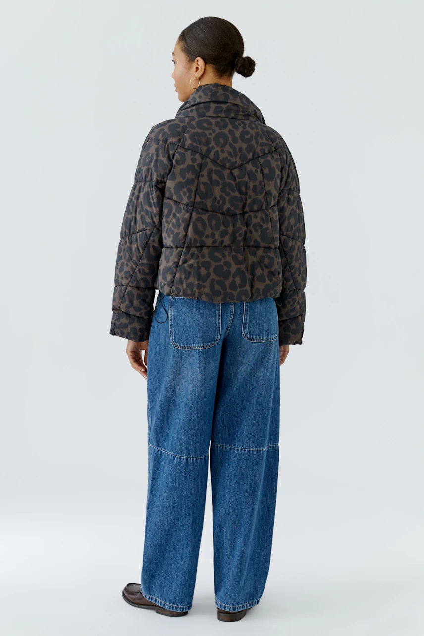 Casual outdoor jacket: Woman in leopard print puffer jacket and wide-leg jeans, viewed from the back.