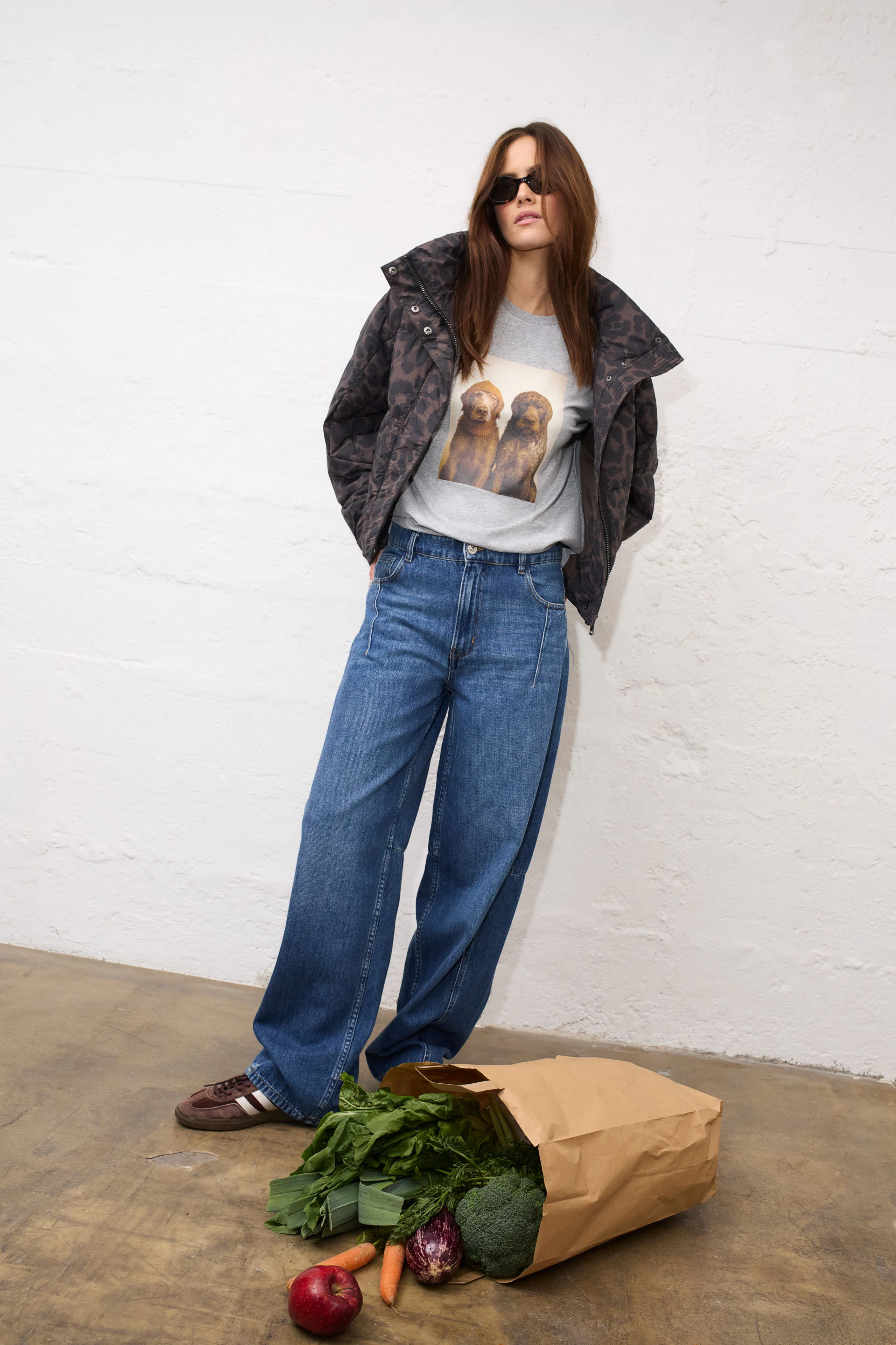 Casual outdoor jacket: Woman in a patterned jacket, graphic tee, and wide jeans, standing confidently.