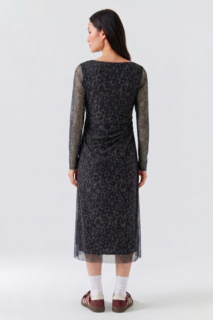 Casual midi dress: Woman in a patterned black midi dress with sheer sleeves, standing confidently.