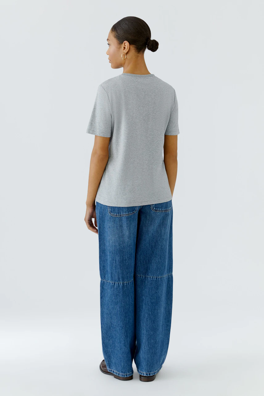 Graues Damen-T-Shirt: Frau von hinten in lockerem T-Shirt und blauer Jeans, schlicht und bequem.