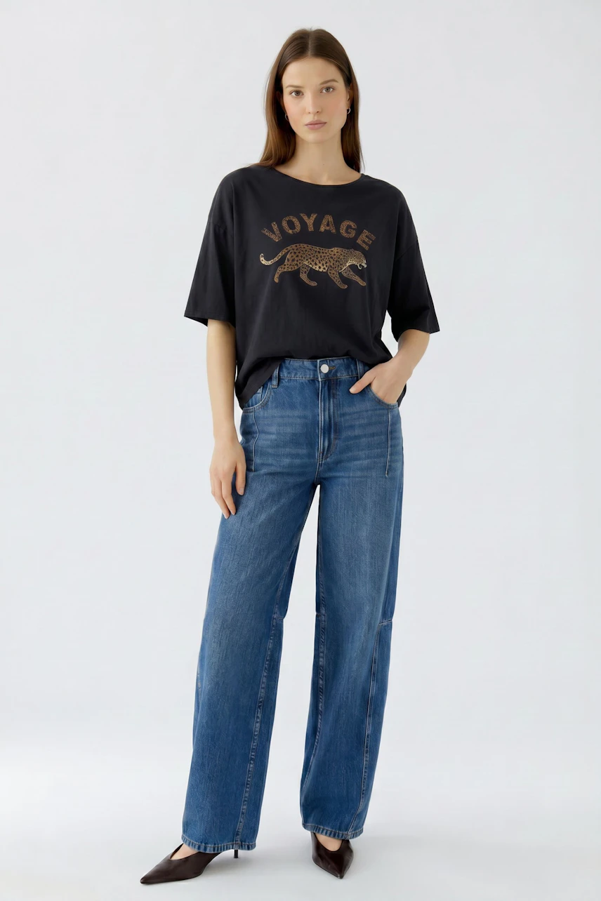 Lässiges Damen-T-Shirt: Frau im schwarzen T-Shirt mit Leopardenmotiv und blauer Jeans steht selbstbewusst.