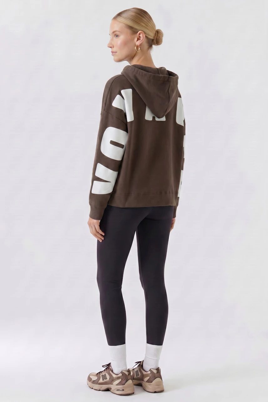 Lässiger Damen-Hoodie: Frau im braunen Hoodie mit weißen Lettern, kombiniert mit schwarzen Leggings.