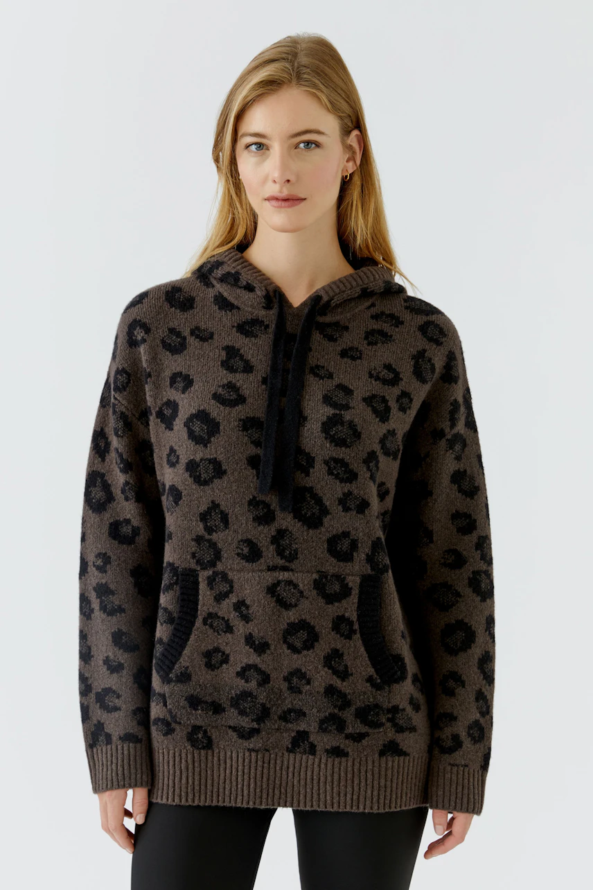 Lässiger Damen-Pullover: Frau im gemusterten Hoodie-Pullover mit Kapuze und Kängurutasche, entspanntes Design.