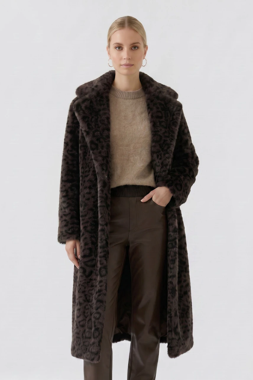 Woman in a leopard print coat, beige pullover, and brown pants, standing confidently.