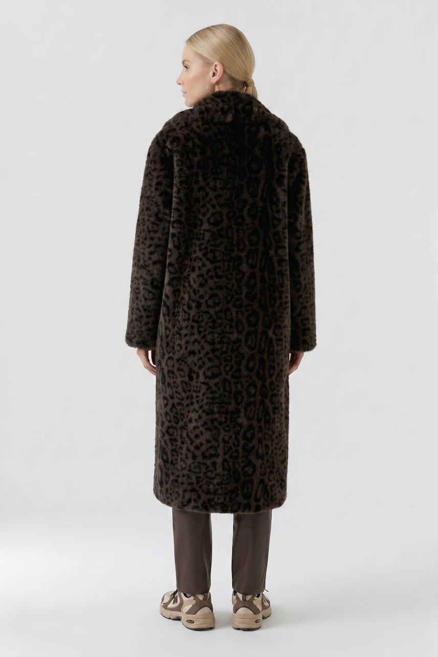 Woman in a long leopard print coat, standing with back view, paired with brown pants and sneakers.