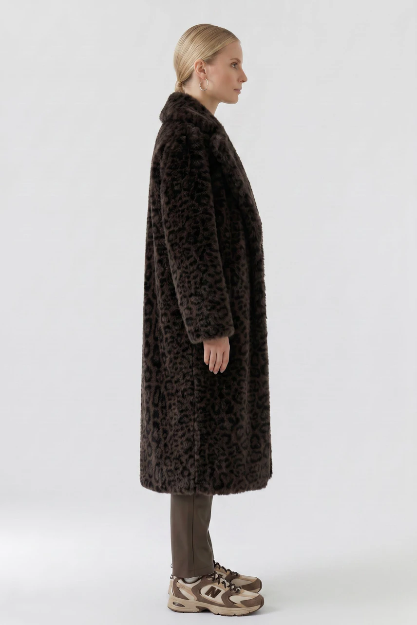 Woman in a long leopard print coat, side view, paired with brown pants and sneakers.