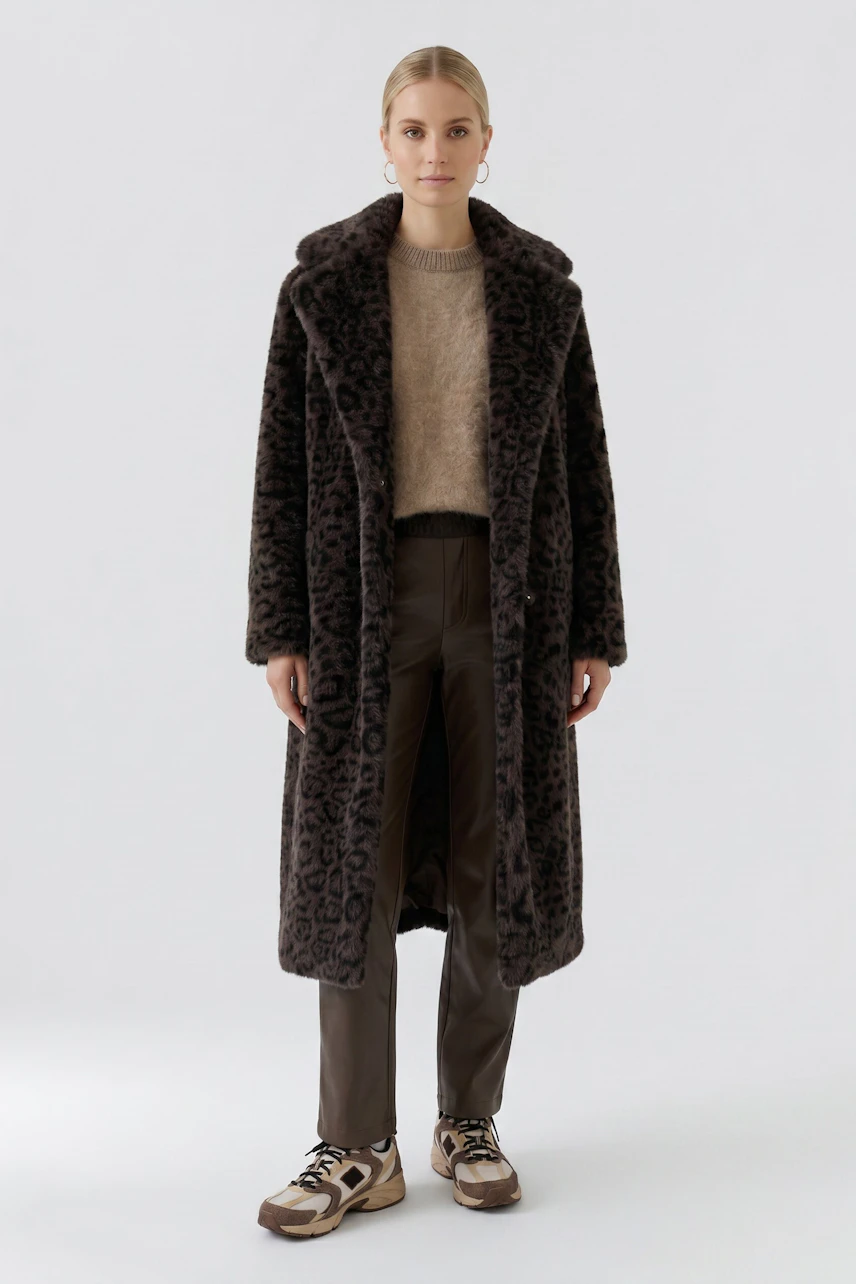 Woman in a leopard print coat, beige pullover, and brown pants, standing confidently.