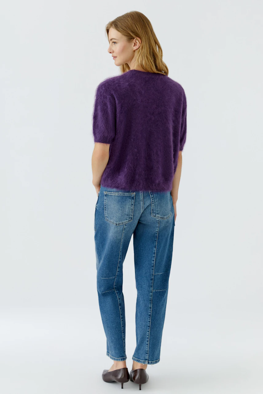 Lässiger Damen-Pullover: Frau im lila Pullover und blauer Jeans, von hinten gesehen, steht entspannt.