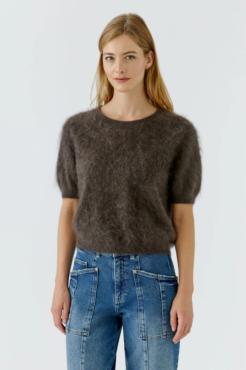 Damen-Pullover: Frau im flauschigen, braunen Pullover mit kurzen Ärmeln und gemusterten Hosen.