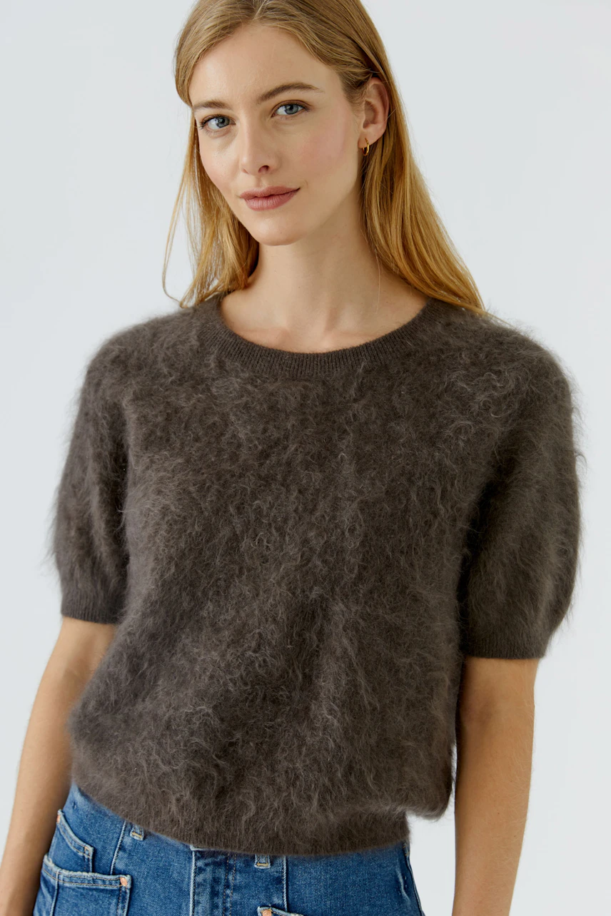 Casual women's pullover: Woman in a fluffy brown pullover with short sleeves and blue jeans, looking relaxed.