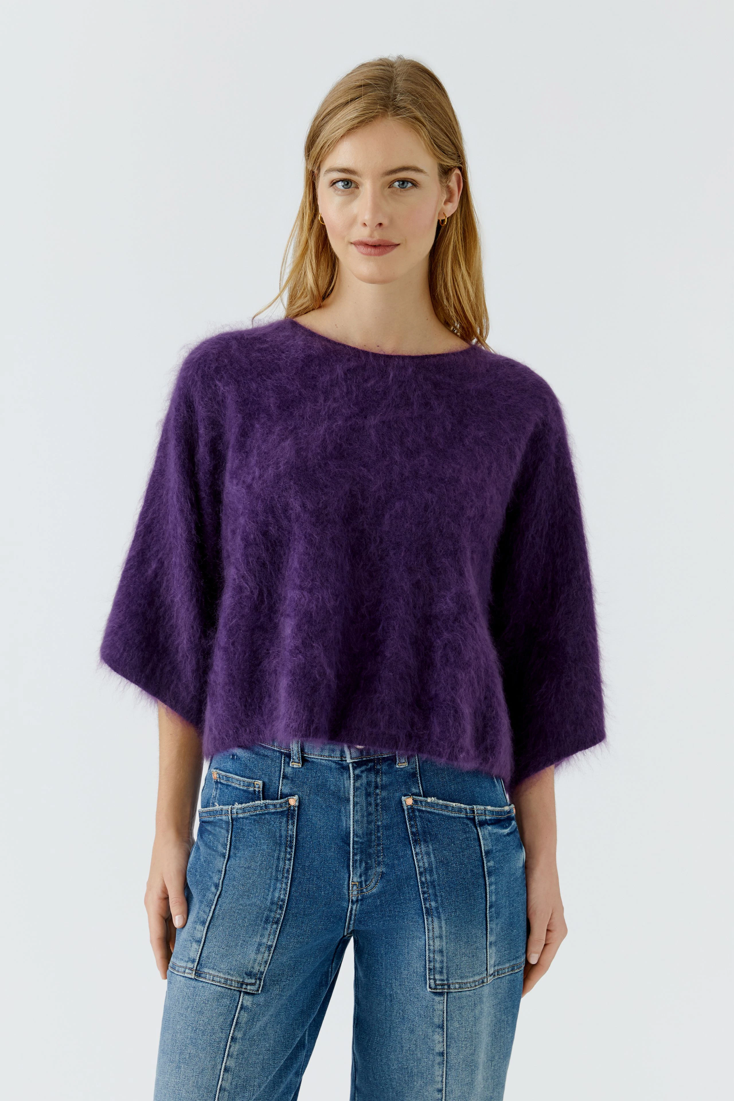 Lässiger Damen-Pullover: Frau im flauschigen lila Pullover und Jeans, lächelt dezent.