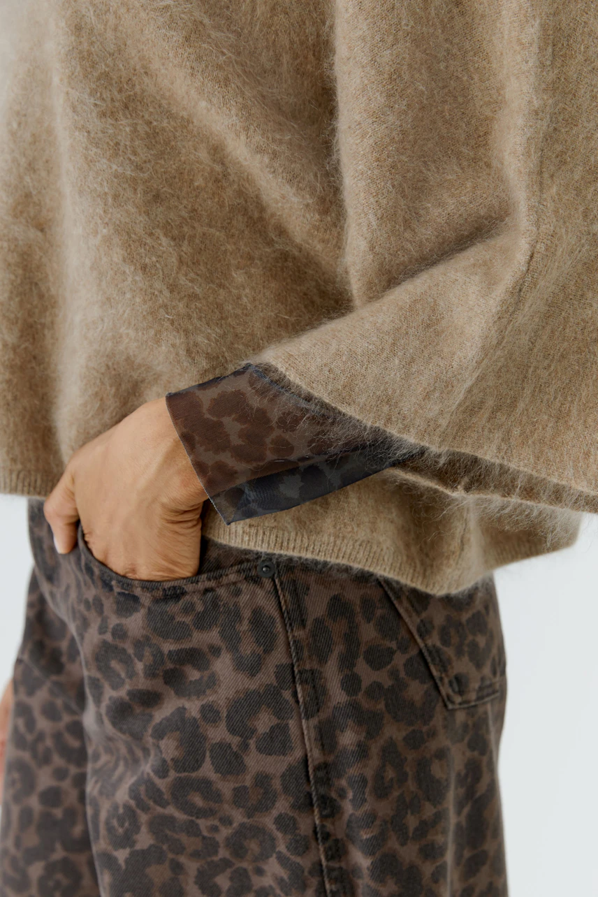 Flauschiger Damen-Pullover: Frau trägt beigen Pullover mit Leopardenmuster-Details und passender Hose.