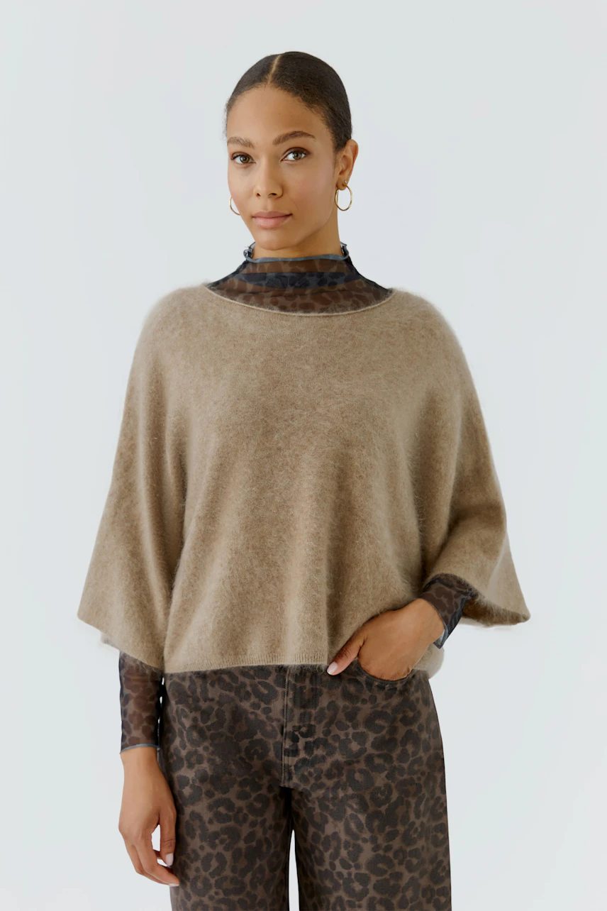 Damen-Pullover: Frau im beigen Pullover über gemustertem Oberteil und Hose, lässiger Look.