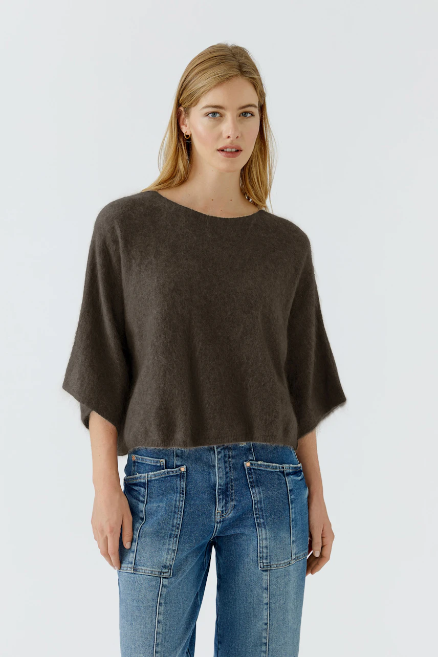 Casual women's pullover: Woman in a cozy brown pullover with wide sleeves and blue jeans, looking relaxed.