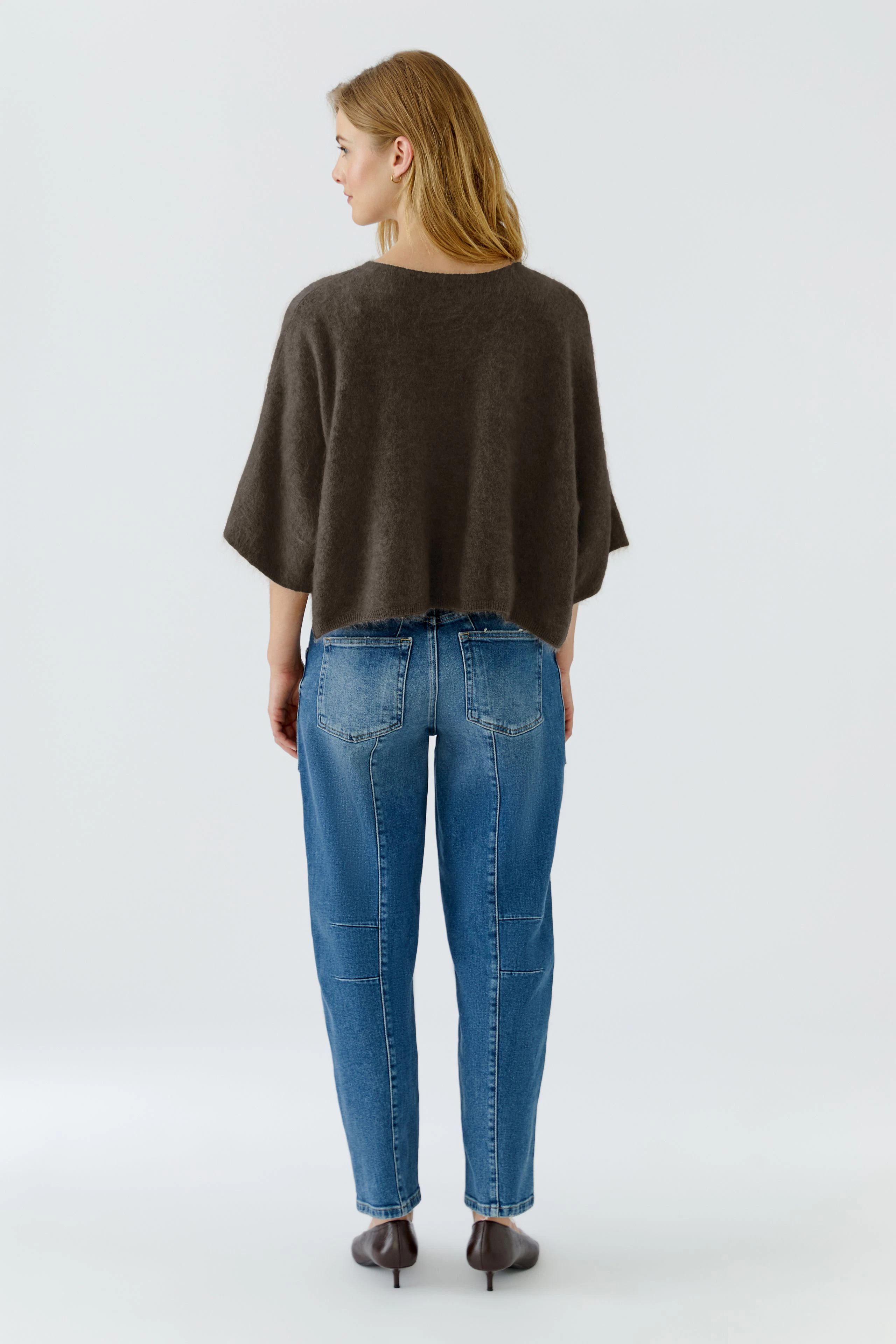 Lässiger Damen-Pullover: Frau im braunen Pullover und blauer Jeans von hinten, entspannt stehend.