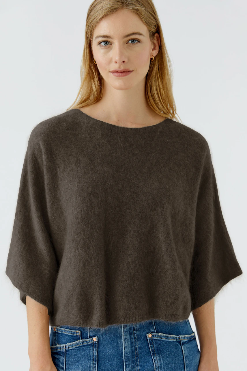 Casual women's pullover: Woman in a cozy brown pullover with wide sleeves and blue jeans, looking relaxed.