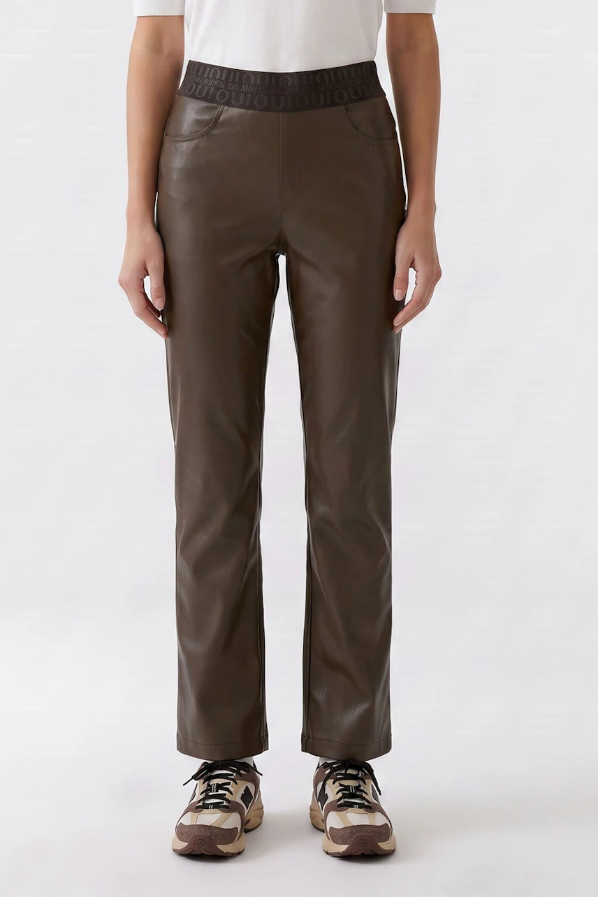 Woman in brown faux leather pants, white top, and sneakers. Casual and stylish look.