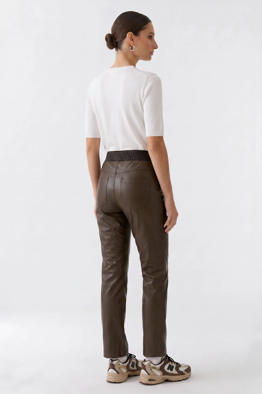 Woman in faux leather pants, white top, and sneakers, showcasing a casual, modern look.