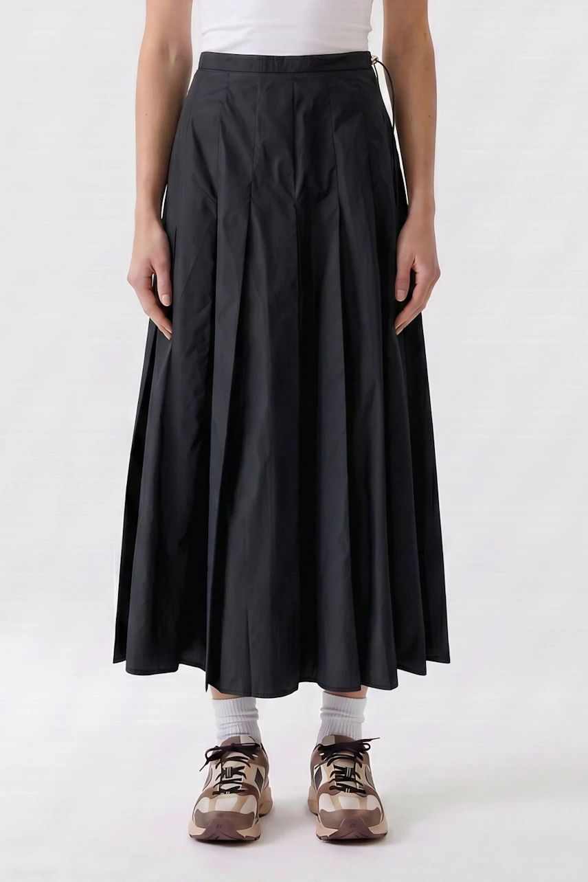 A-line skirt: Woman in a long black A-line skirt, white top, and sneakers, standing casually.
