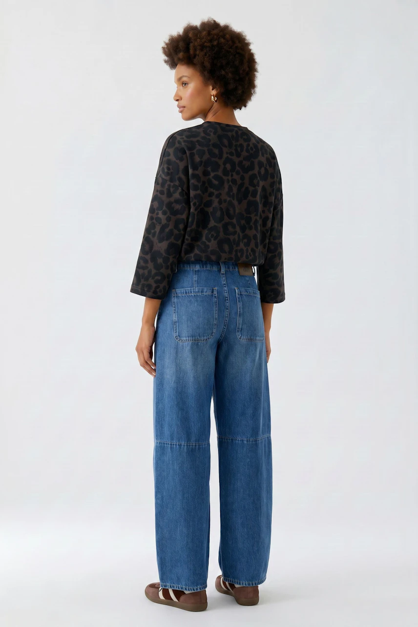 Casual sweatshirt: Woman in leopard print sweatshirt and wide-leg jeans, standing confidently.