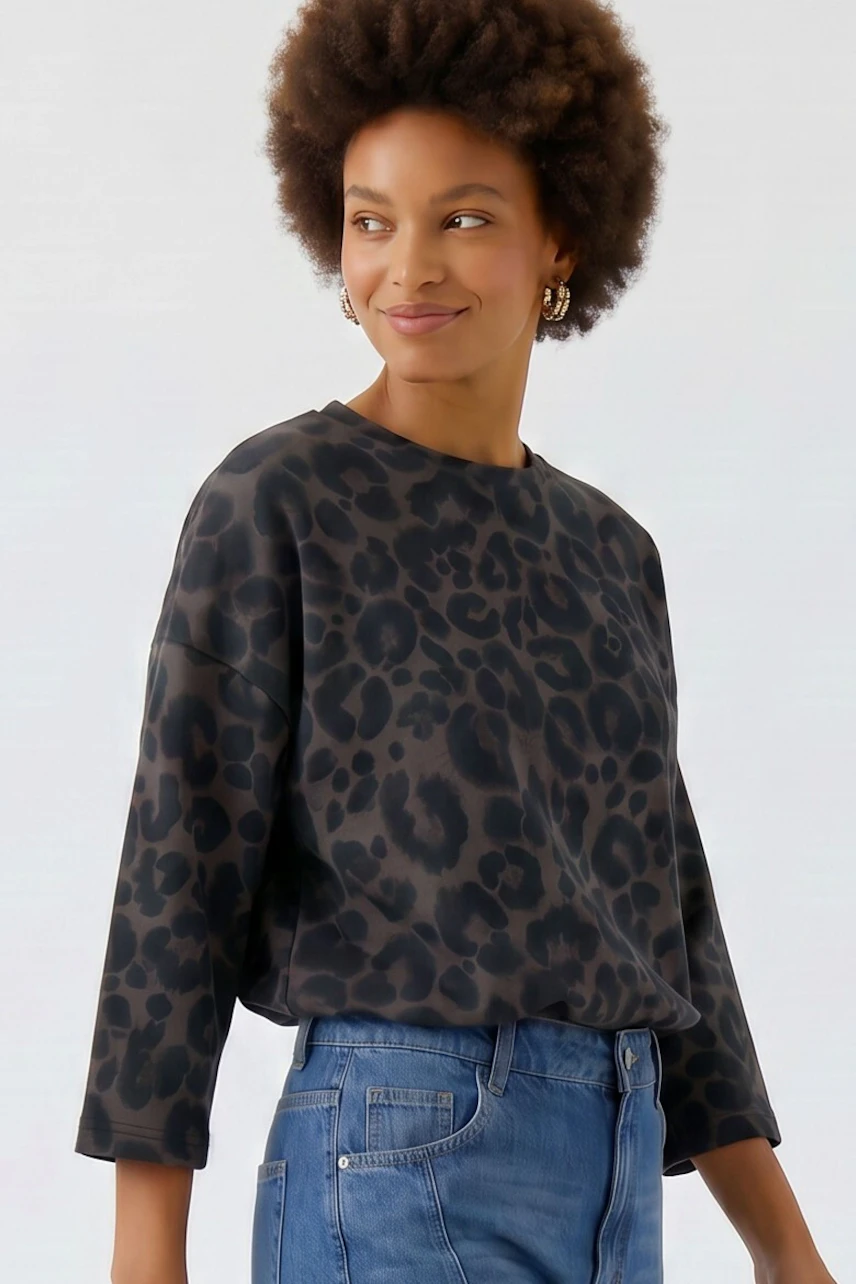 Lässiges Damen-Sweatshirt: Frau im schwarzen Sweatshirt mit Leopardenmuster und blauer Jeans lächelt entspannt.