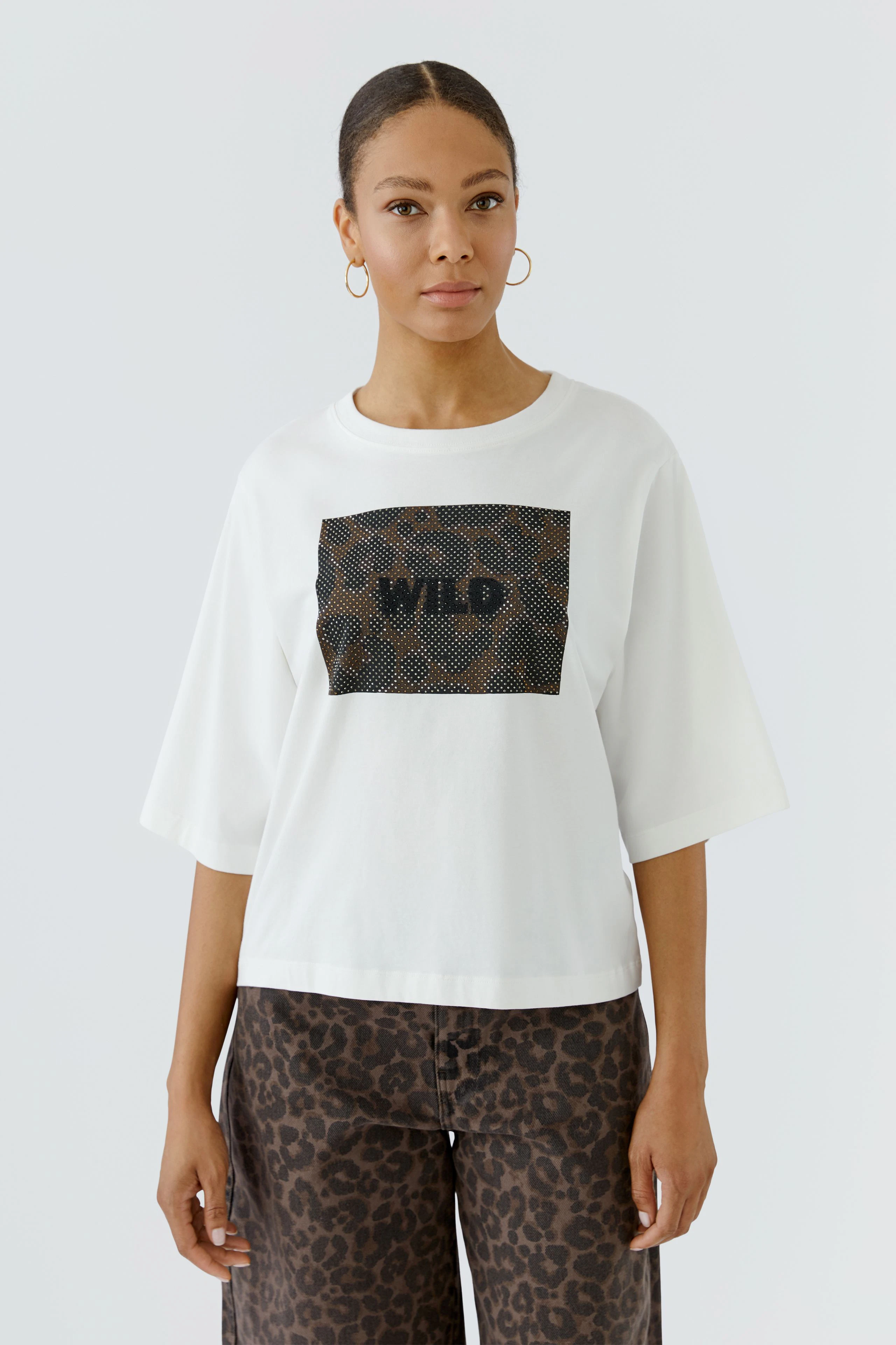 Weißes Damen-T-Shirt: Frau trägt locker geschnittenes T-Shirt mit "WILD"-Print und gemusterter Hose.