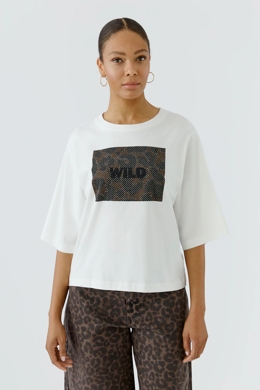 Weißes Damen-T-Shirt: Frau trägt locker geschnittenes T-Shirt mit "WILD"-Print und gemusterter Hose.