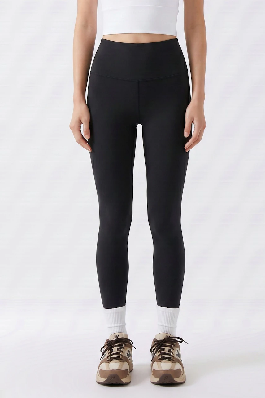 Schwarze Leggings: Frau in schlichten, schwarzen Leggings, kombiniert mit weißem Top und Sneakers.