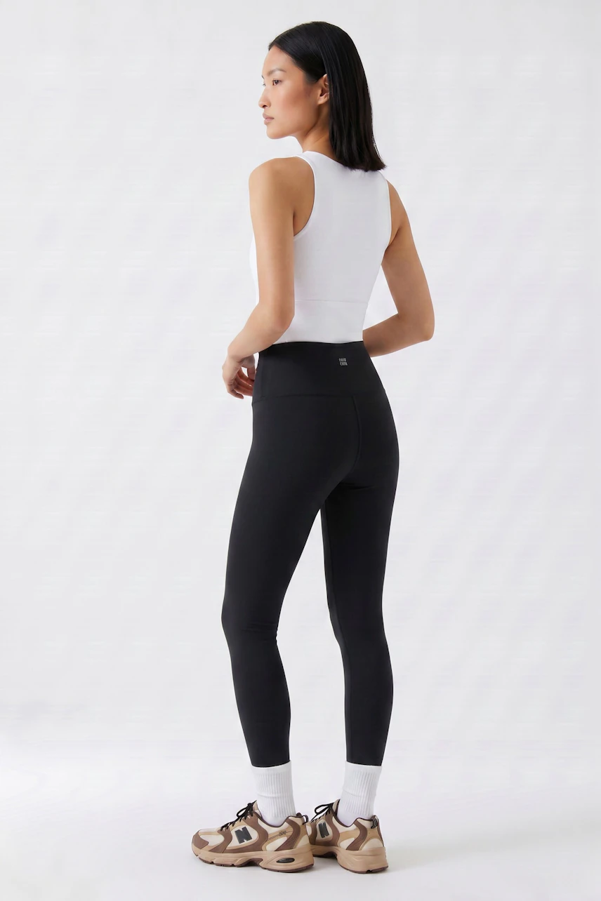 Schwarze Leggings: Frau im weißen Top und schwarzen Leggings, seitlich stehend, mit sportlichen Sneakers.