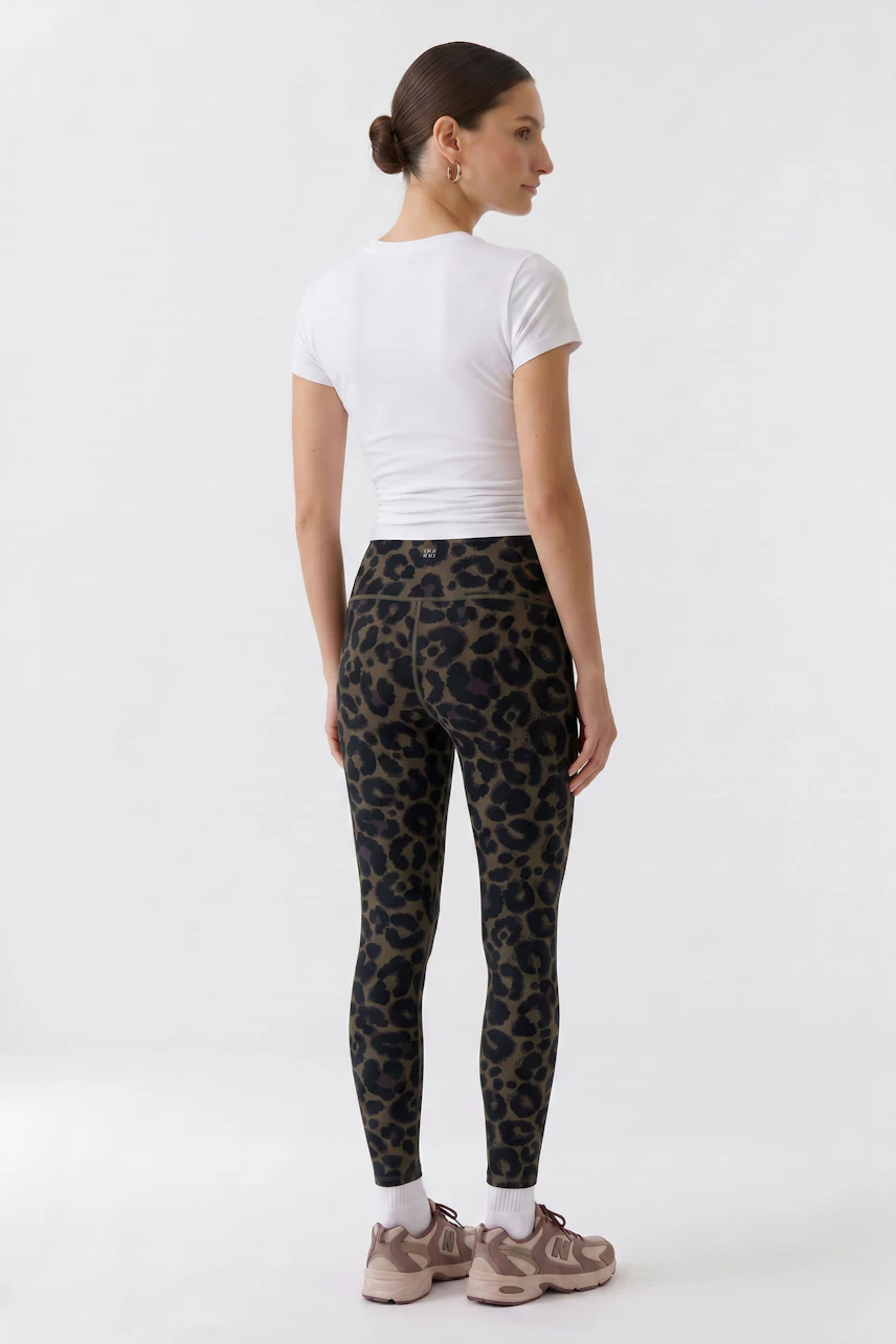 Damen-Leggings: Frau in gemusterten Leggings und weißem T-Shirt, seitlich stehend, mit sportlichen Schuhen.