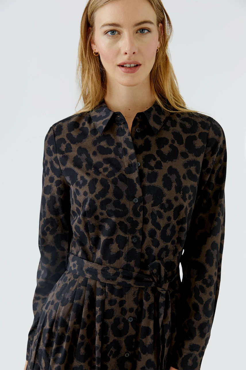 Frau im Midikleid mit Leopardenmuster, lässig und modern, blickt direkt in die Kamera.