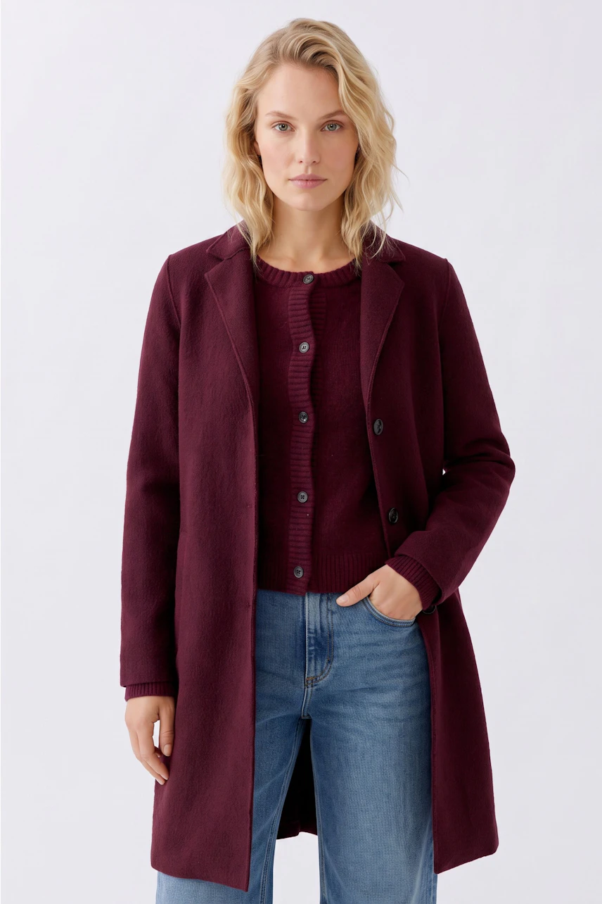 Modern women's wool coat: A woman in a burgundy coat over a red sweater and jeans stands confidently.