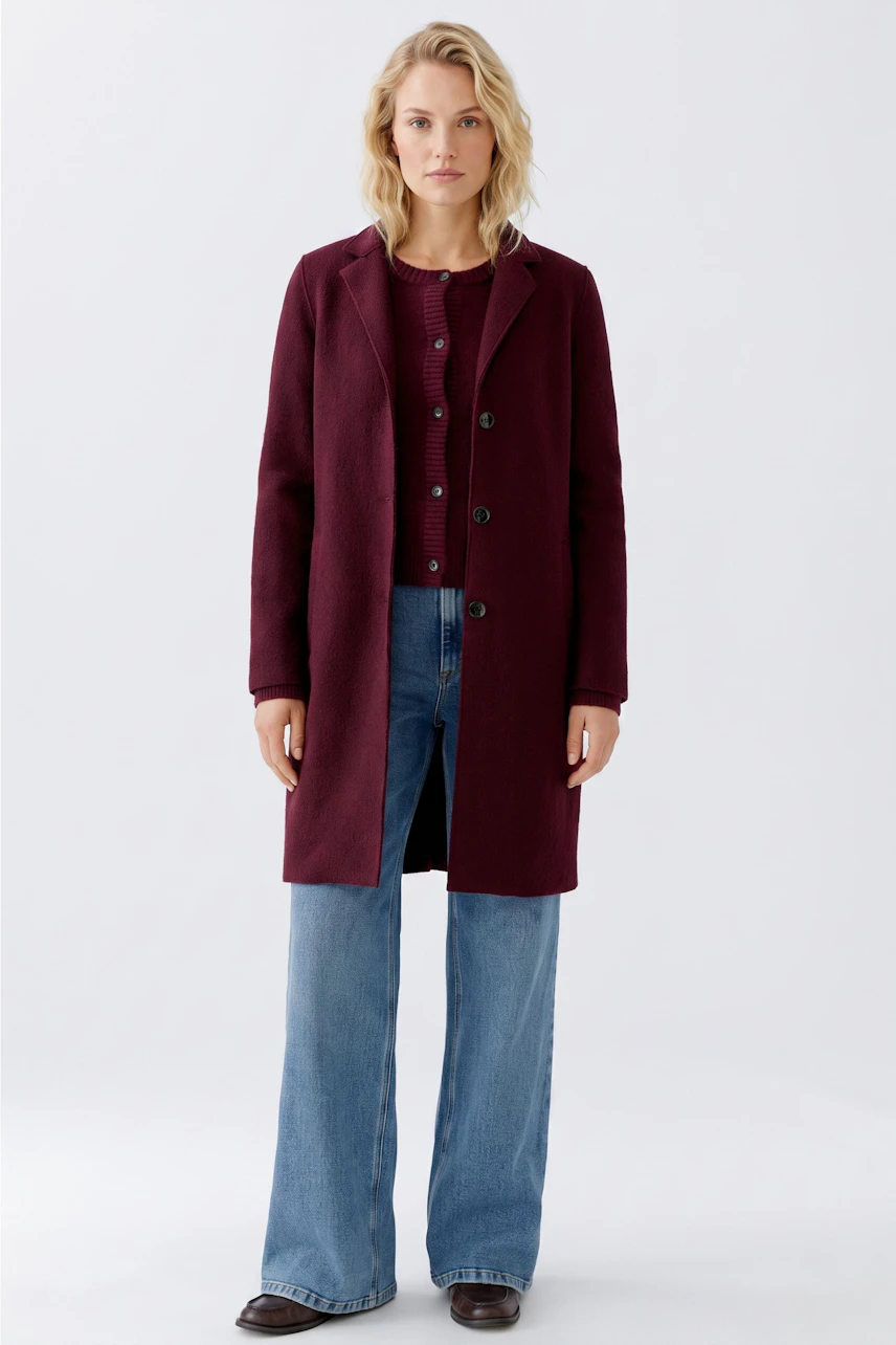 Modern women's wool coat: A woman in a burgundy coat over a matching cardigan and wide-leg jeans.