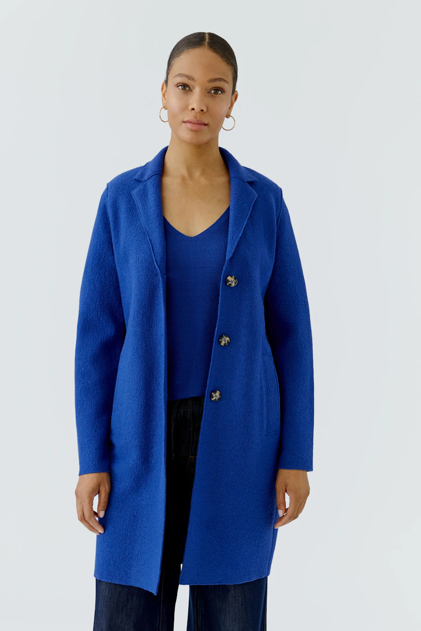Blauer Wollmantel: Frau im offenen Mantel mit V-Ausschnitt-Top und dunkler Hose, schlicht und modern.