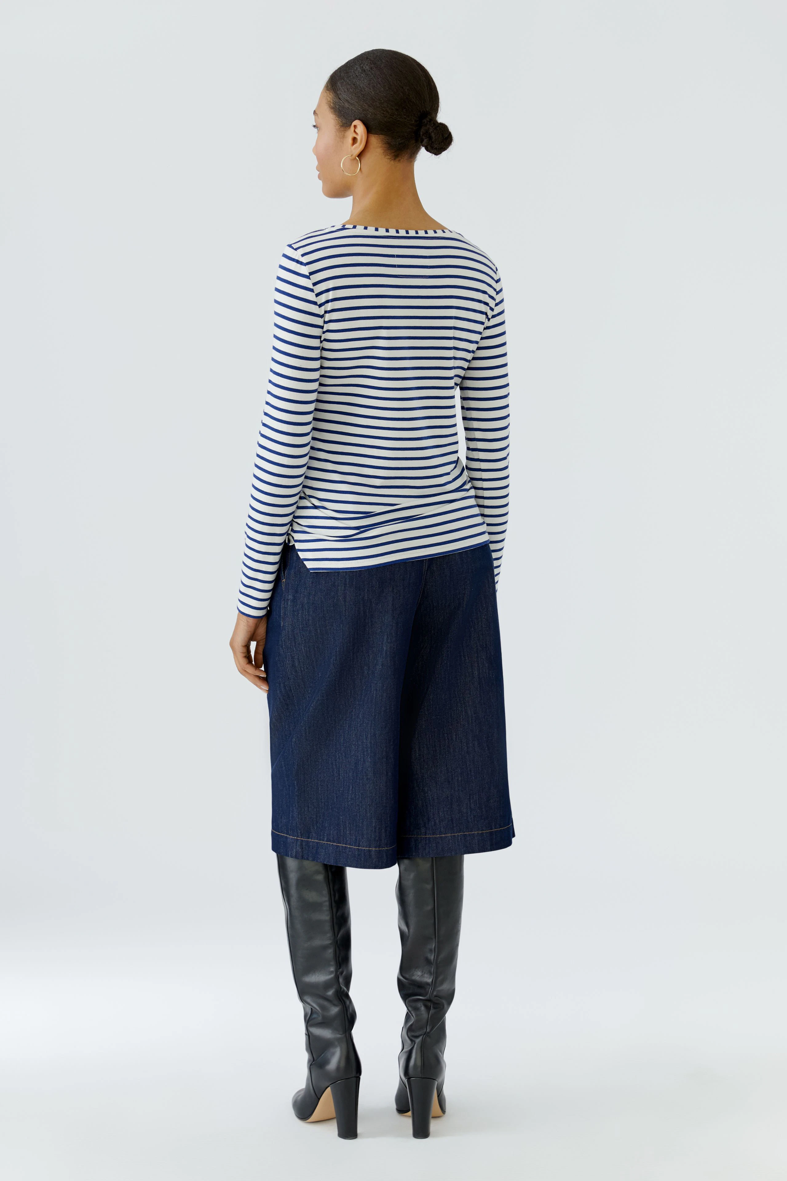 Striped long-sleeve shirt: Woman in casual navy culottes and knee-high boots, viewed from the back.