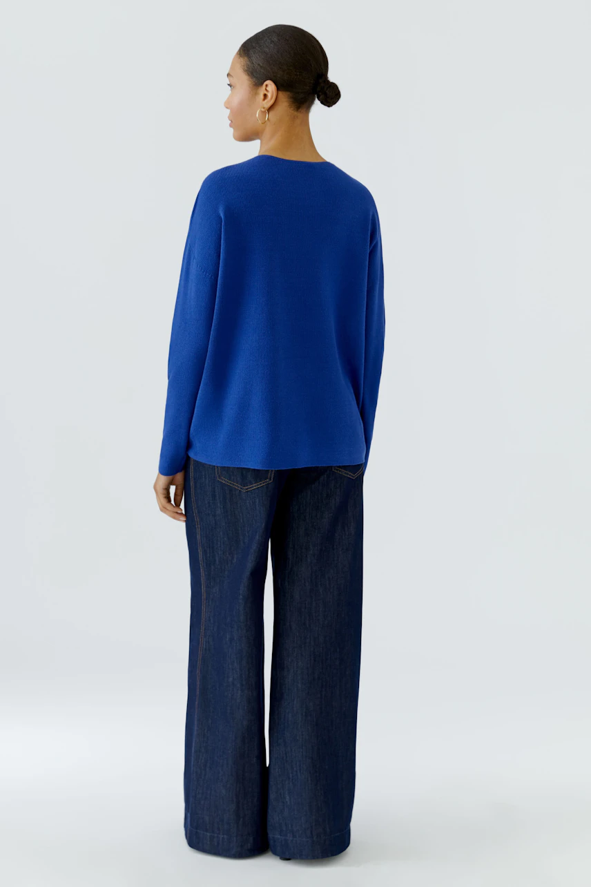 Casual blue pullover: Woman in a relaxed fit pullover and wide-leg jeans, viewed from the back.