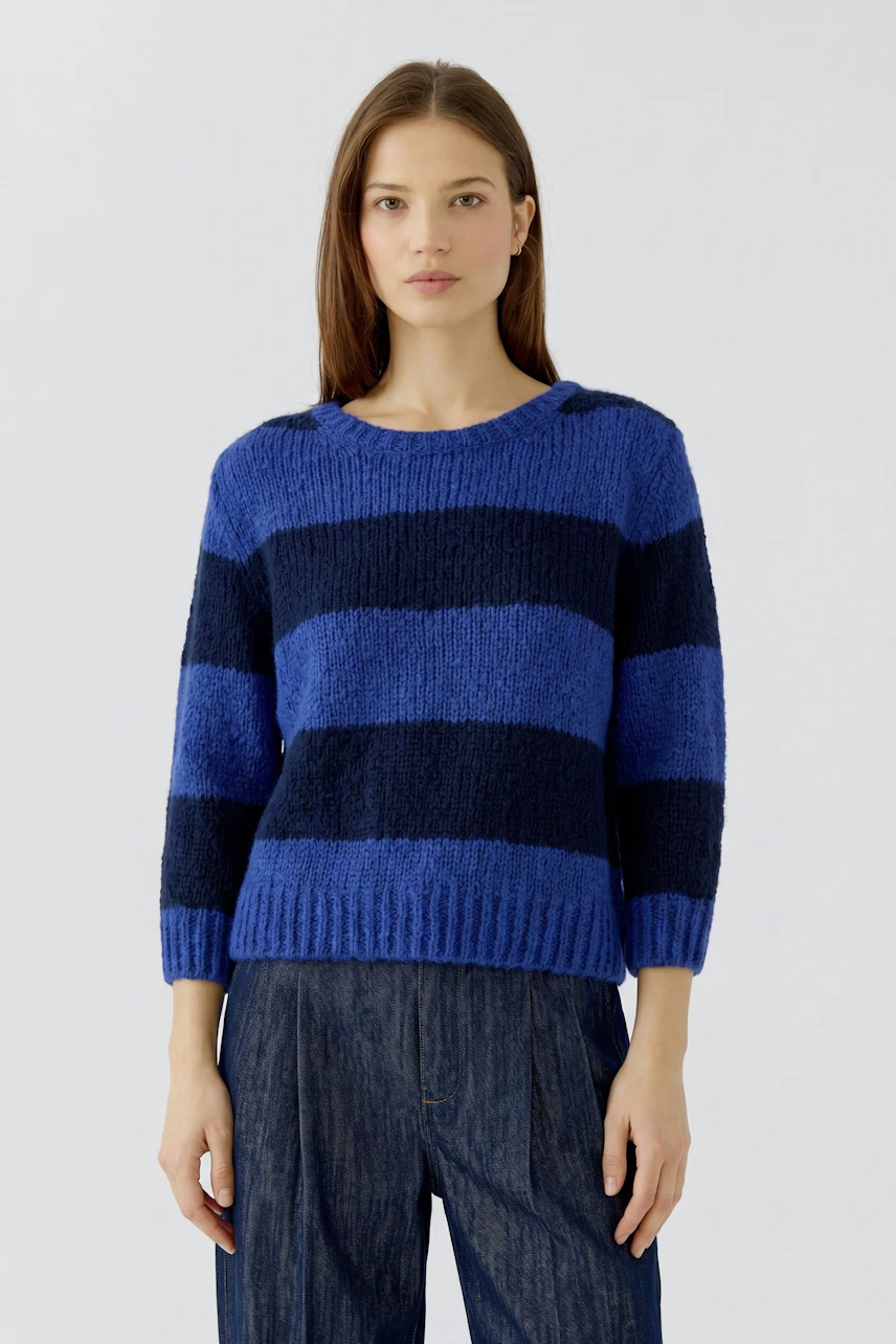 Casual women's pullover: Woman in a blue and black striped pullover with relaxed fit, paired with jeans.