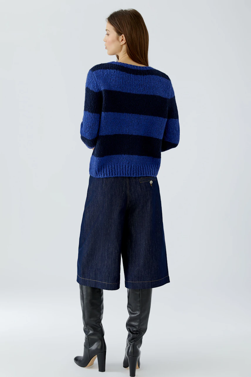 Casual women's pullover: Woman in blue and black striped pullover, denim culottes, and knee-high boots.