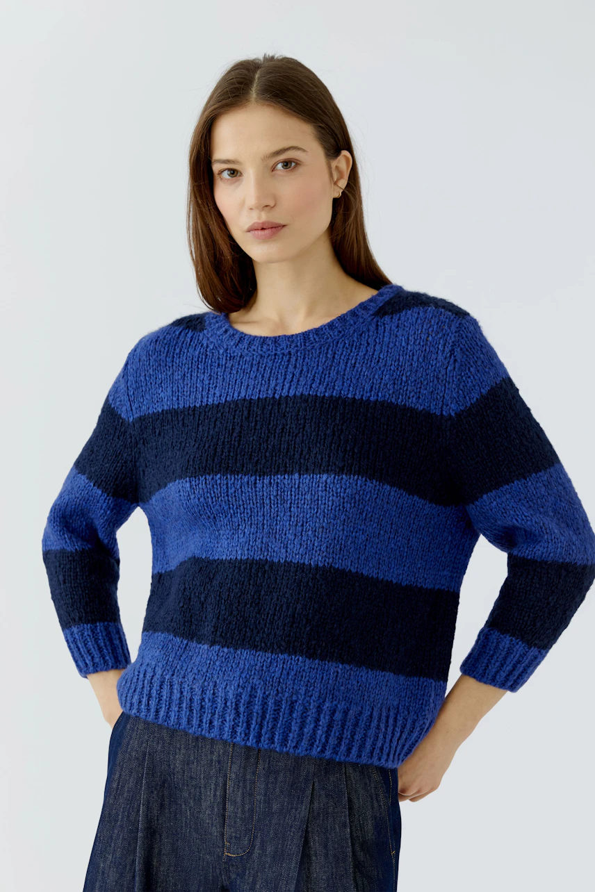 Casual women's pullover: Woman in a blue and navy striped pullover with relaxed fit, hands on hips.