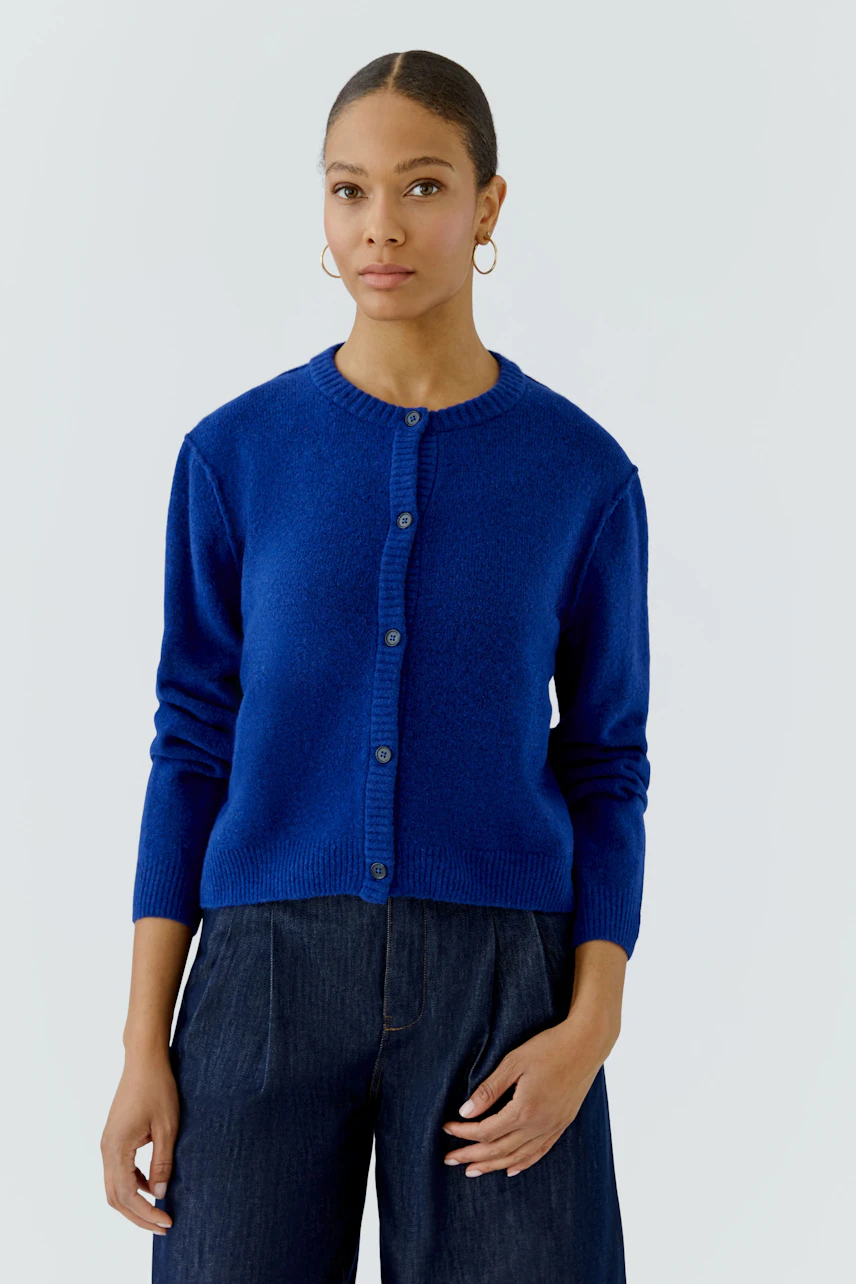 Blue cardigan: Woman in a vibrant blue knit cardigan with button-up front, paired with dark jeans.