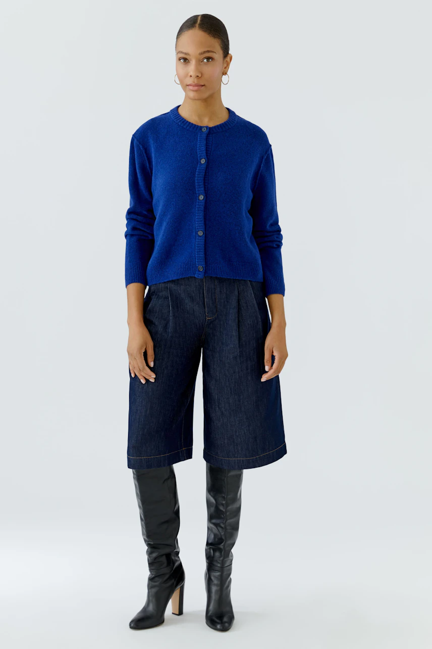 Woman in blue cardigan, denim culottes, and black boots. Casual and stylish look.