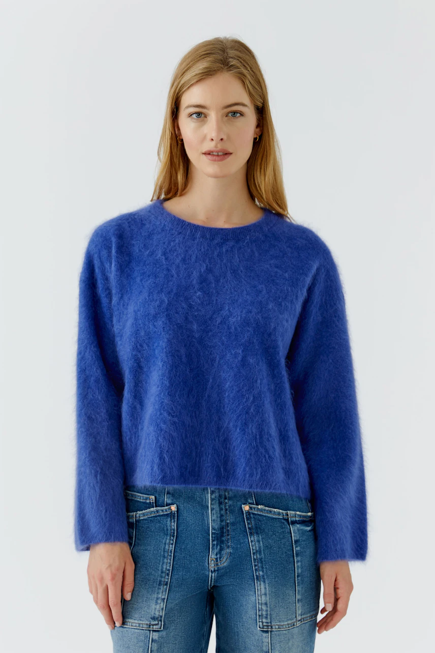 Frau im blauen Pullover aus flauschigem Material, kombiniert mit lässiger Jeans, schaut direkt in die Kamera.