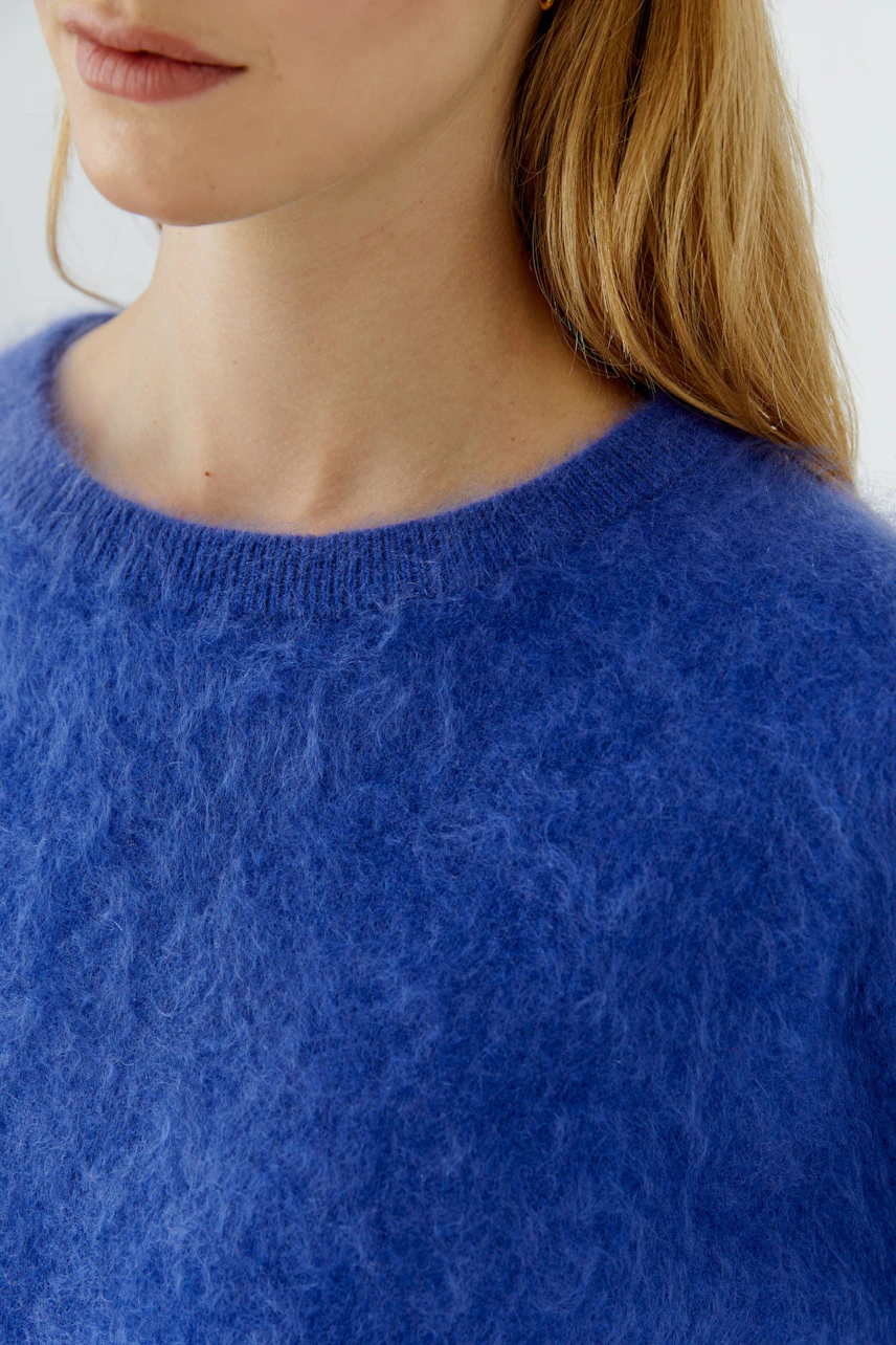 Flauschiger Damen-Pullover: Frau trägt blauen Pullover aus weichem Material, ideal für kühle Tage.