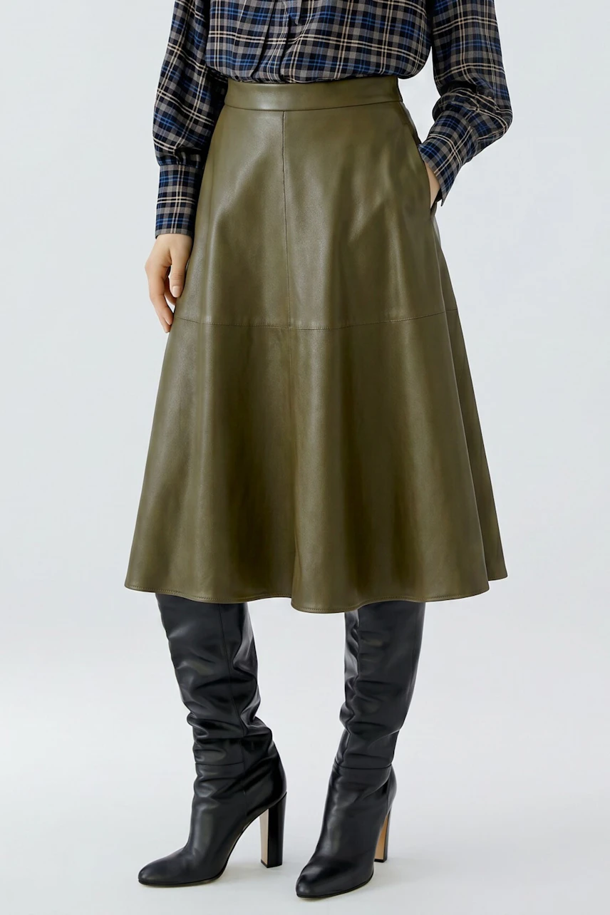 A-line skirt: Woman in olive leather skirt with plaid shirt and black boots, showcasing a chic look.