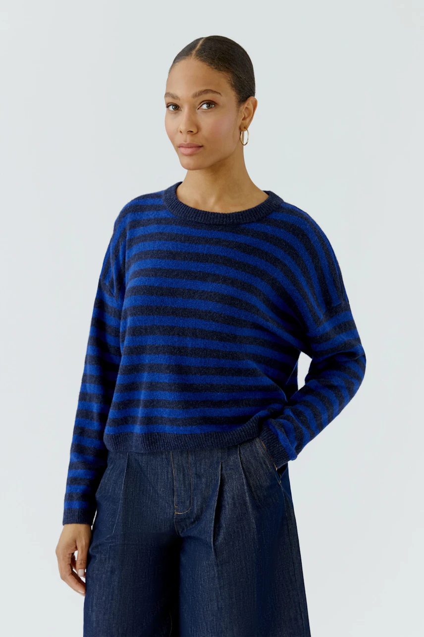 Casual women's pullover: Woman in blue striped pullover and dark jeans, standing confidently.