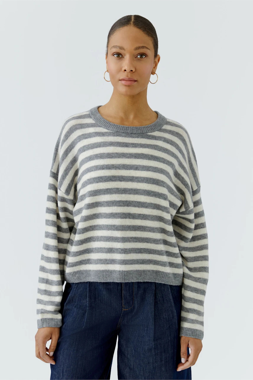 Casual women's pullover: Woman in a striped grey and white pullover with relaxed fit, paired with jeans.