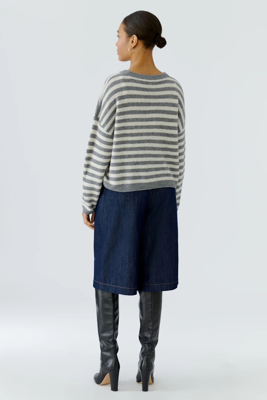 Casual pullover: Woman in striped pullover, denim culottes, and tall black boots, viewed from the back.