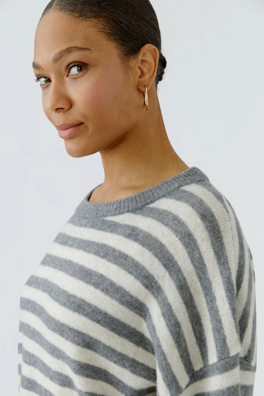 Striped pullover: Woman in a cozy, gray and white striped pullover, looking confidently to the side.