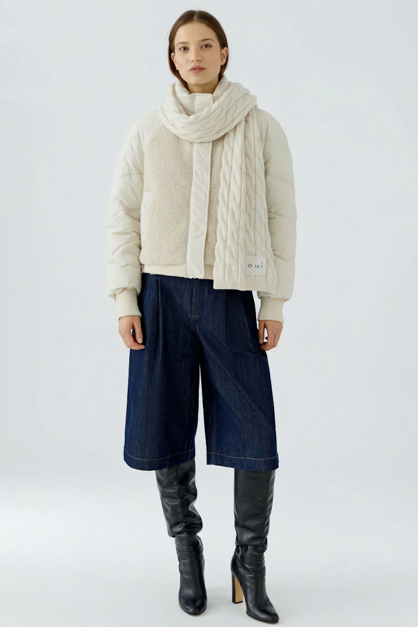 Woman in cozy scarf: Cream knit scarf paired with a casual jacket and denim culottes, exuding warmth.