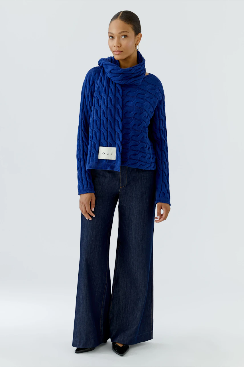 Blauer Schal: Frau trägt blauen Schal mit passendem Pullover und weiter Jeans, lässiger Look.
